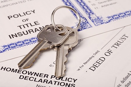 Keys on top of deed, title, homeowner policy, and property records